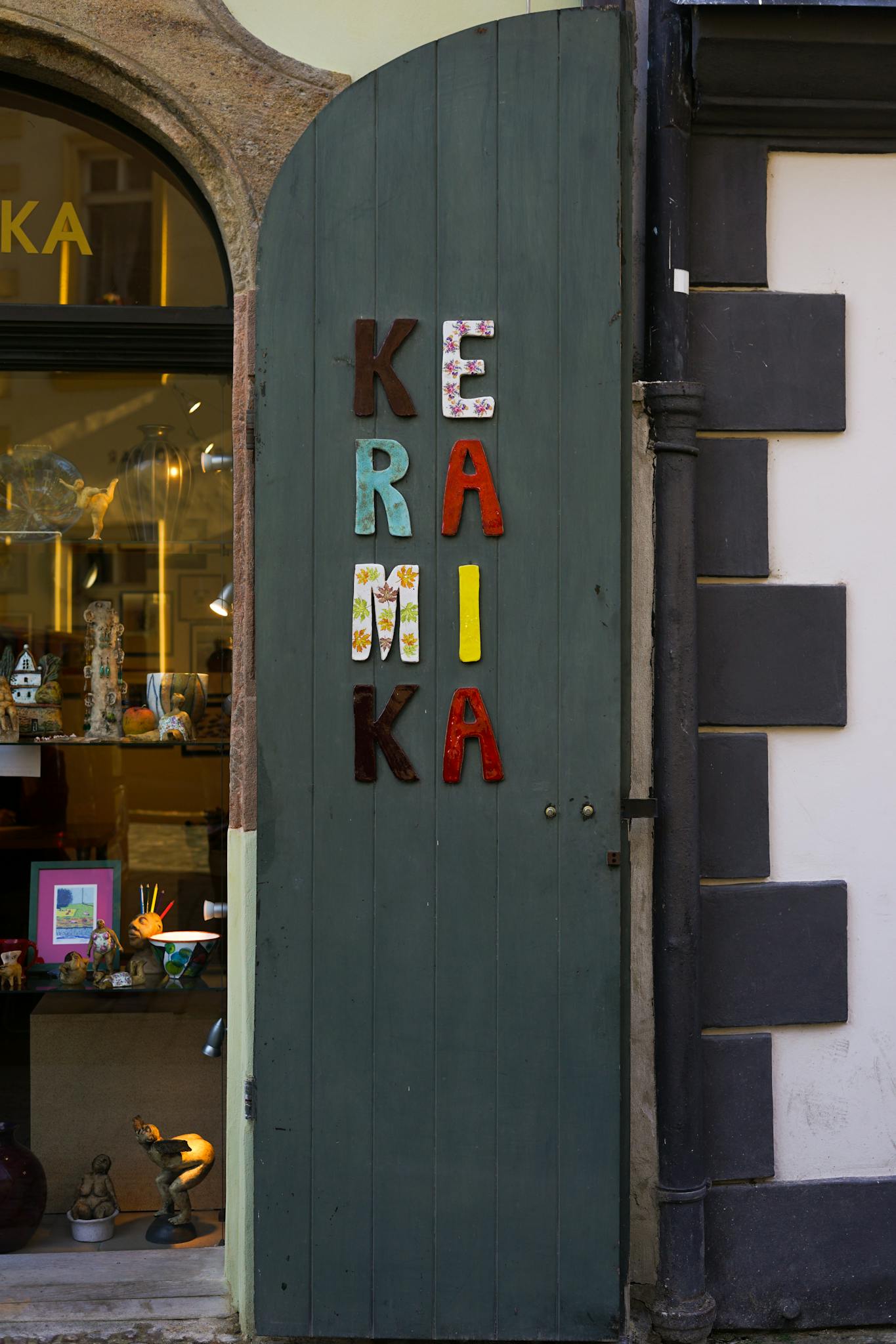 A vibrant display of ceramic craft shop entrance with colorful letters on green wooden door.